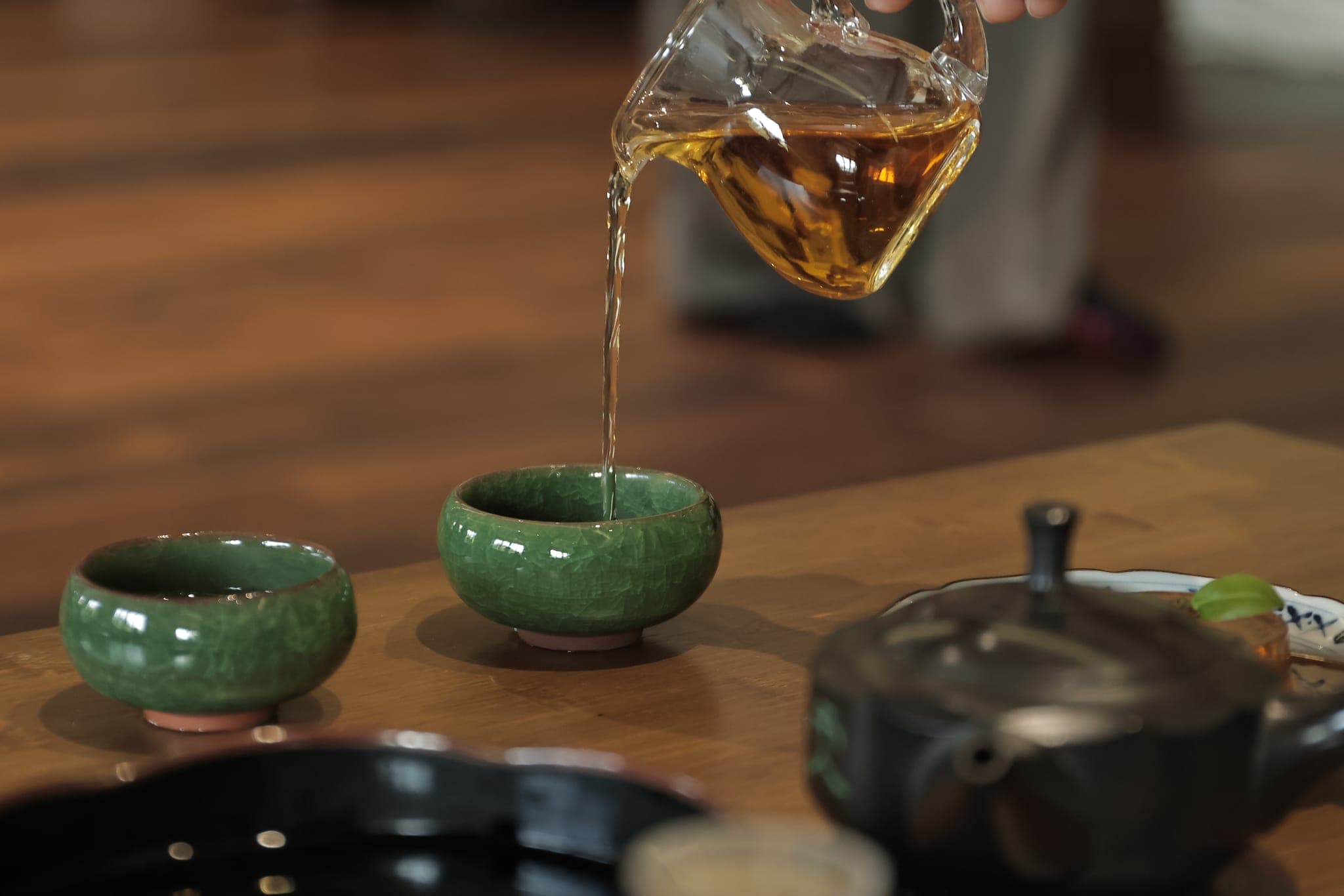 Rót trà vàng từ bình thủy tinh vào chén sứ xanh
