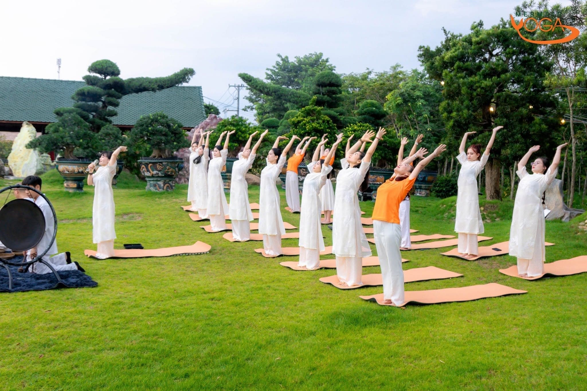 Nhóm người tập yoga trên bãi cỏ vườn, mặc áo dài trắng